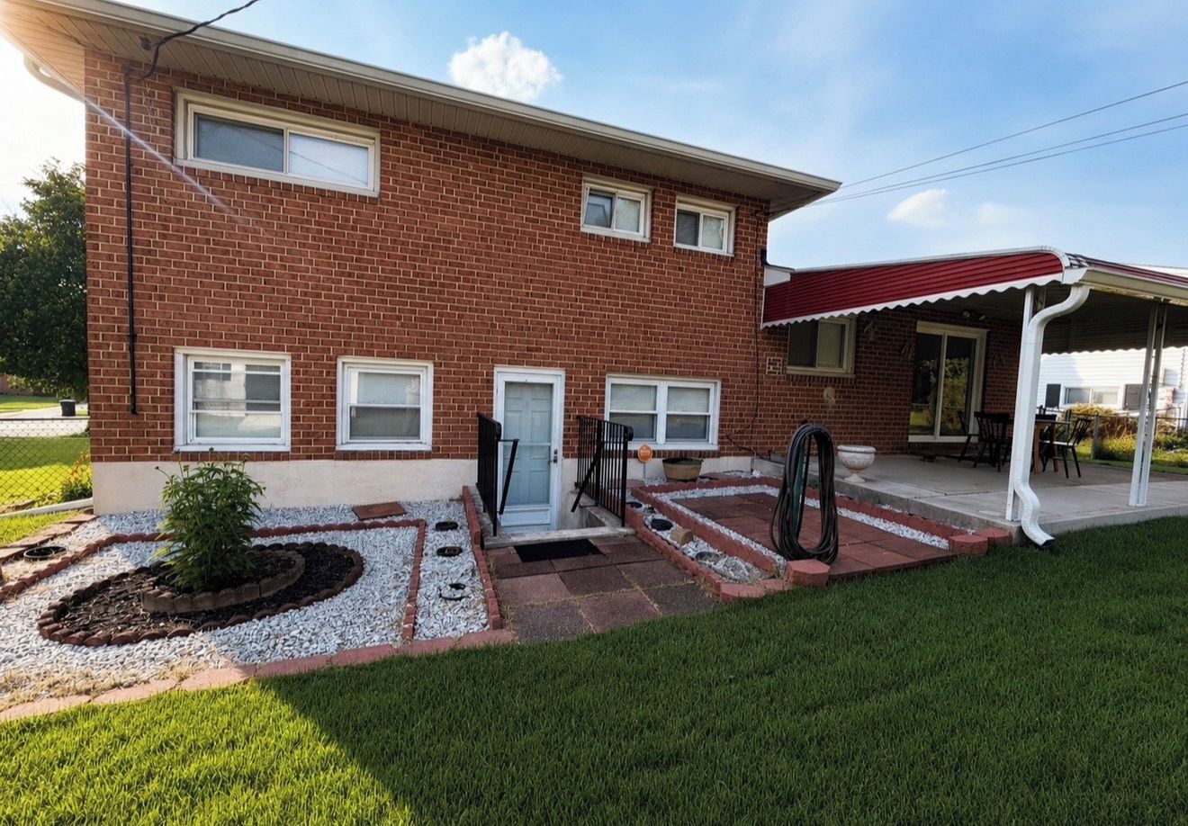 A two-story brick house with a front porch, a covered patio, and a well-maintained lawn.