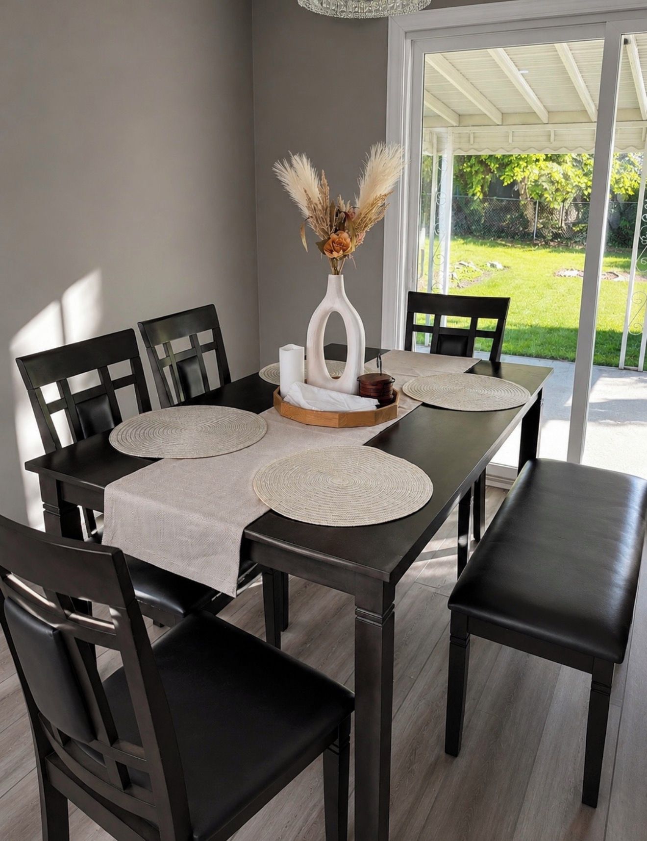 Un coin repas avec une table dressée pour quatre personnes, agrémenté d’un vase contenant des fleurs séchées, d’une bougie et d’un plateau en bois.