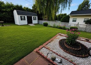 Une pelouse bien entretenue, avec un petit abri de jardin et un parterre fleuri.