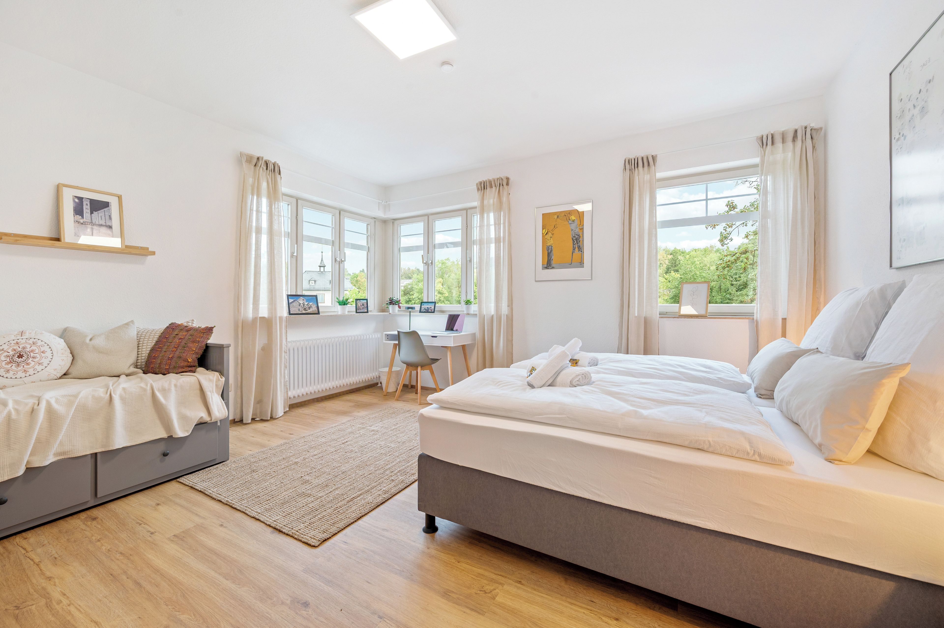 Ein modernes Schlafzimmer mit einem großen Bett, einem Schreibtisch und Blick ins Grüne.