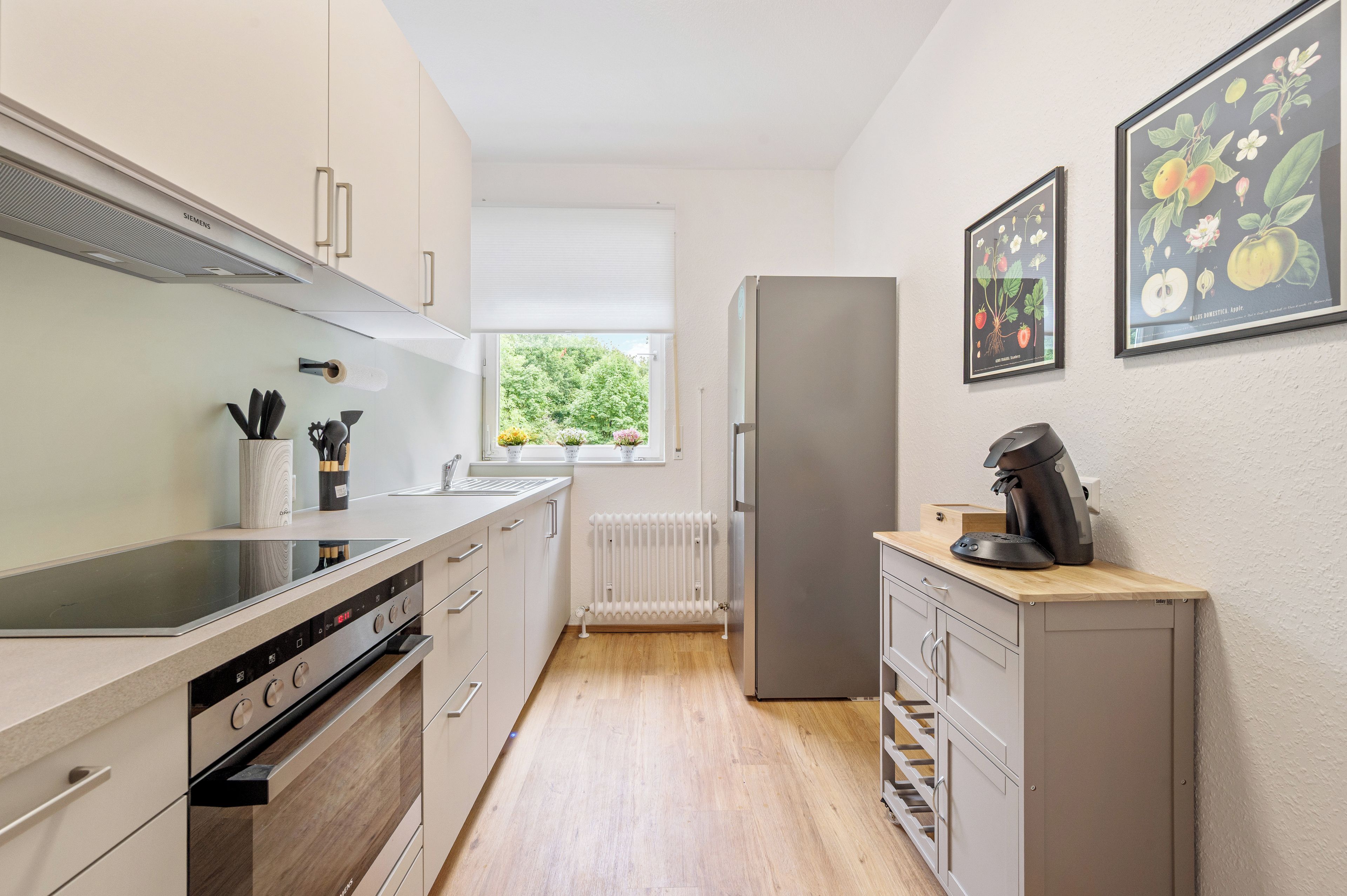 Eine moderne Küche mit Einbauofen, Kühlschrank und Fenster mit Blick auf Grünflächen.