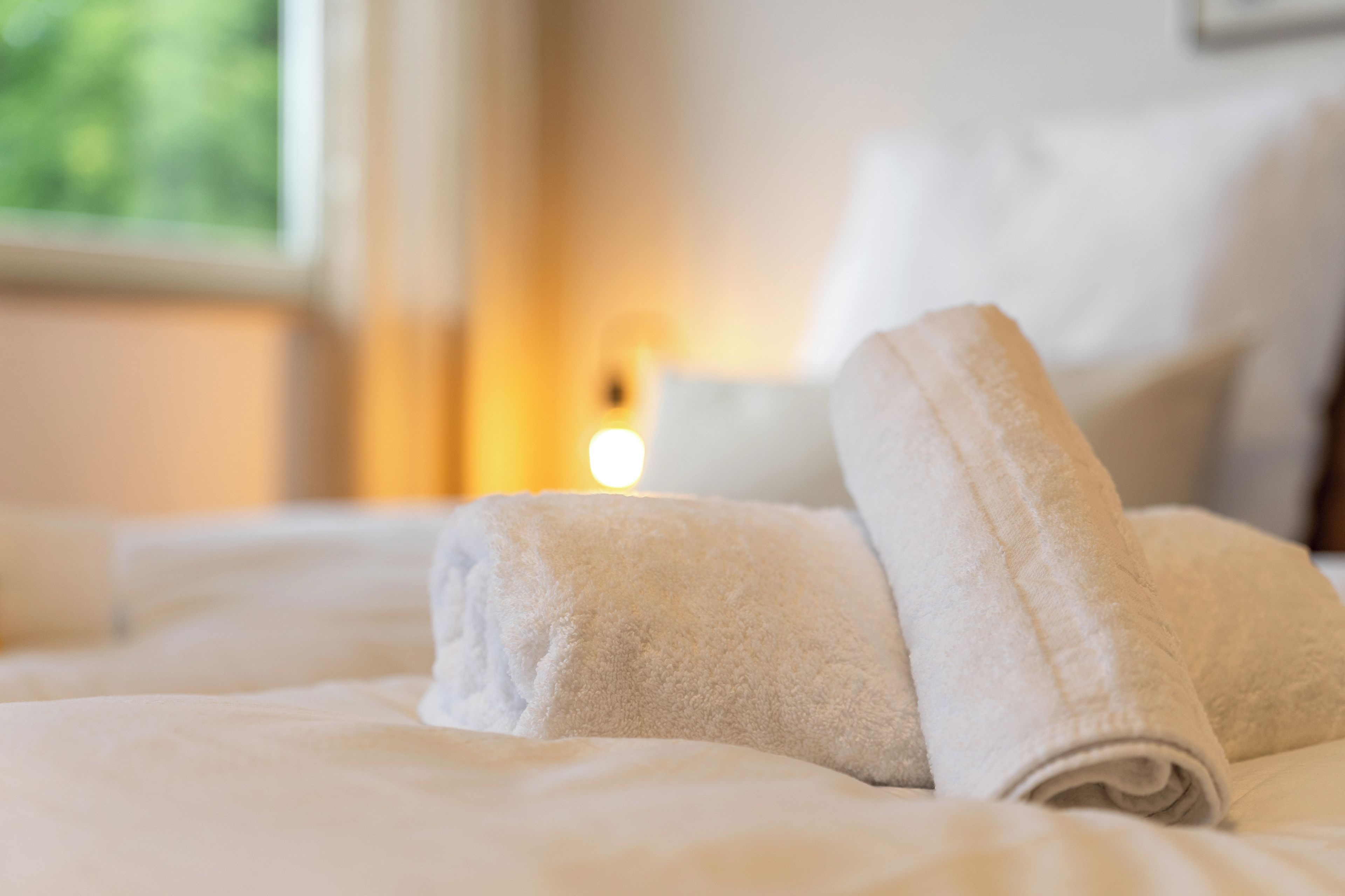 Ein ordentlich gemachtes Bett mit aufgerollten Handtüchern und einer Nachttischlampe.
