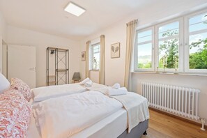 A hotel room with a bed, a radiator, a window with curtains, and a view of greenery outside. - Vacation Rental on Lake Trappensee (Heilbronn)