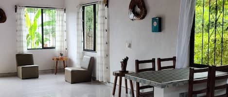 A spacious room with a dining table and chairs, a ceiling fan, and large windows with curtains.