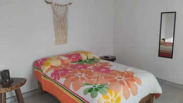 A bed with a floral bedspread, a macrame wall hanging, a small wooden stool, and a mirror on the wall.