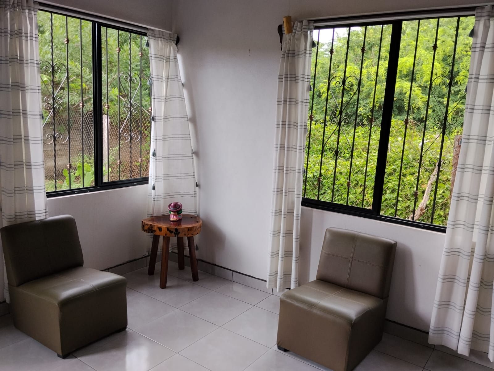 A room with two leather chairs, a small wooden table with a decorative item, and large windows with curtains.