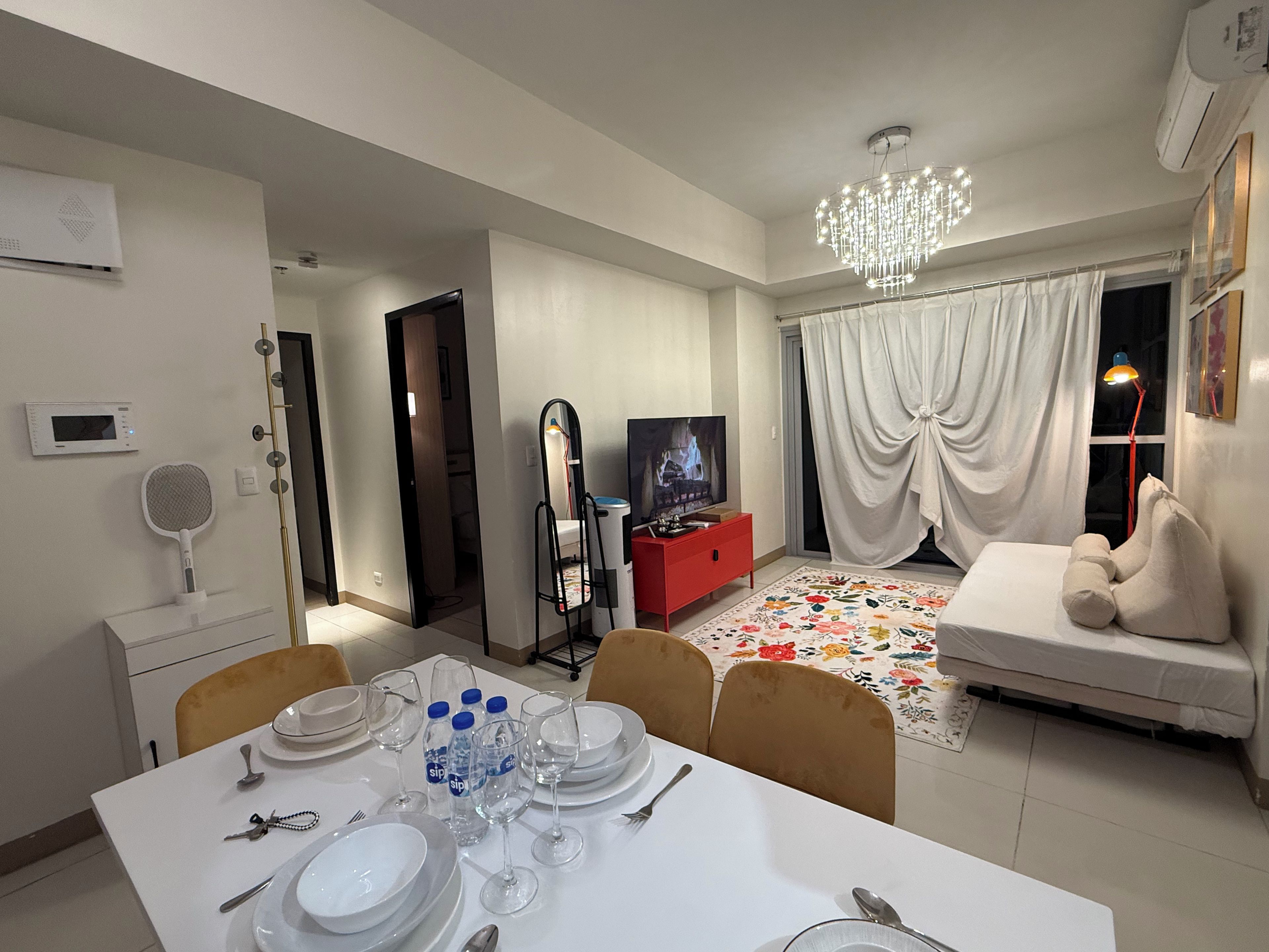 A dining area with a table set for four, a television, a sofa, and a decorative rug.