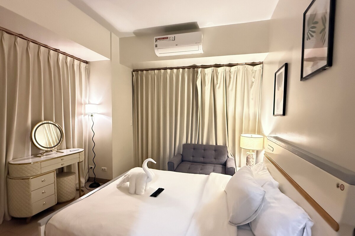 Ett hotellrum med en säng, en sminkbord med spegel, en stol, en lampa och gardiner.