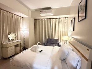 Ett hotellrum med en säng, en sminkbord med spegel, en stol, en lampa och gardiner.