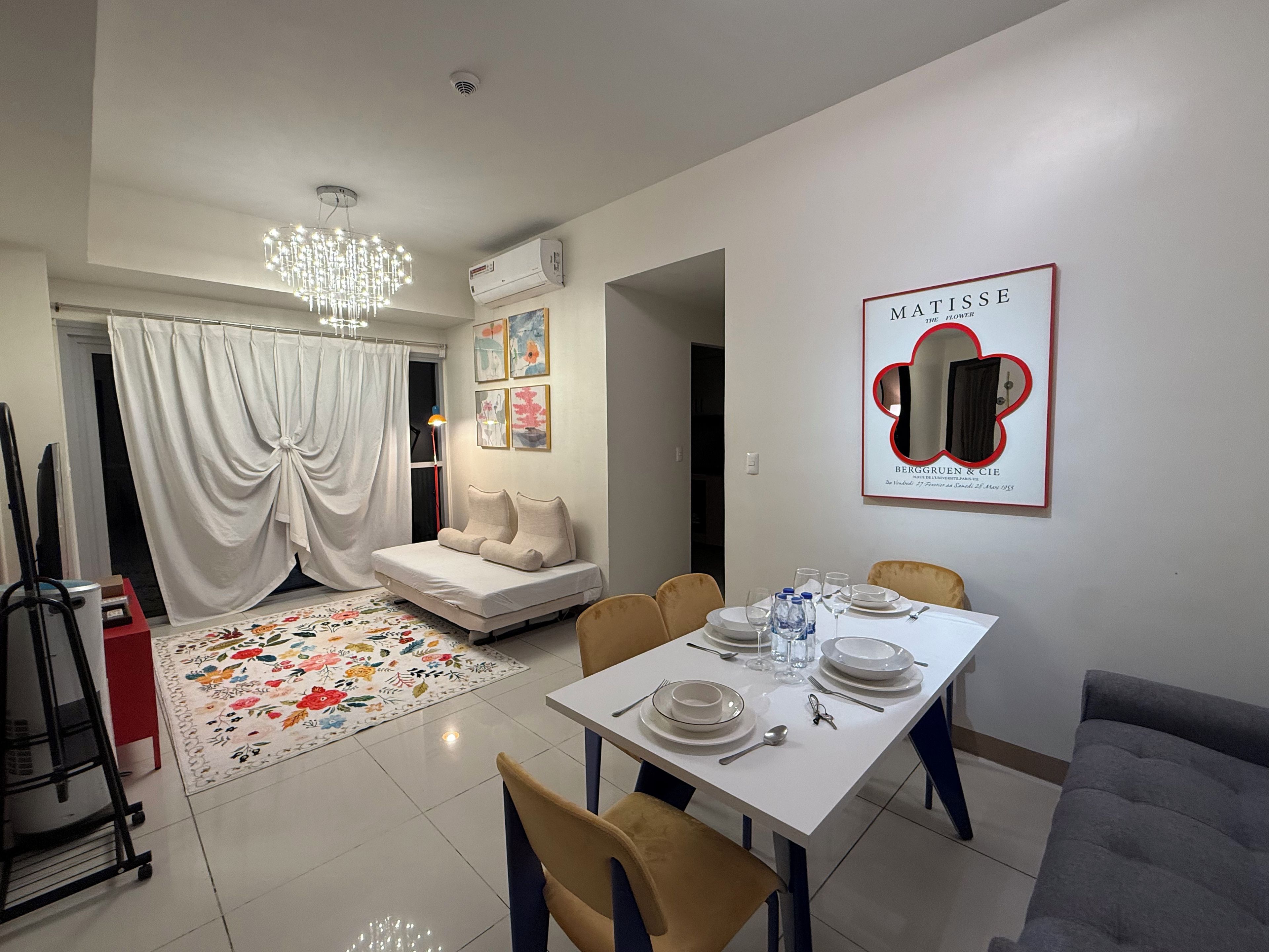 A modern living room with a sofa, dining table set for four, and a chandelier.