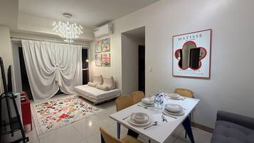 A modern living room with a sofa, dining table set for four, and a chandelier.