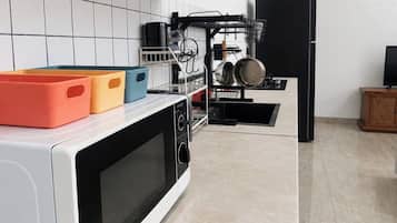 A kitchen with a microwave, a dish rack, and a black refrigerator.