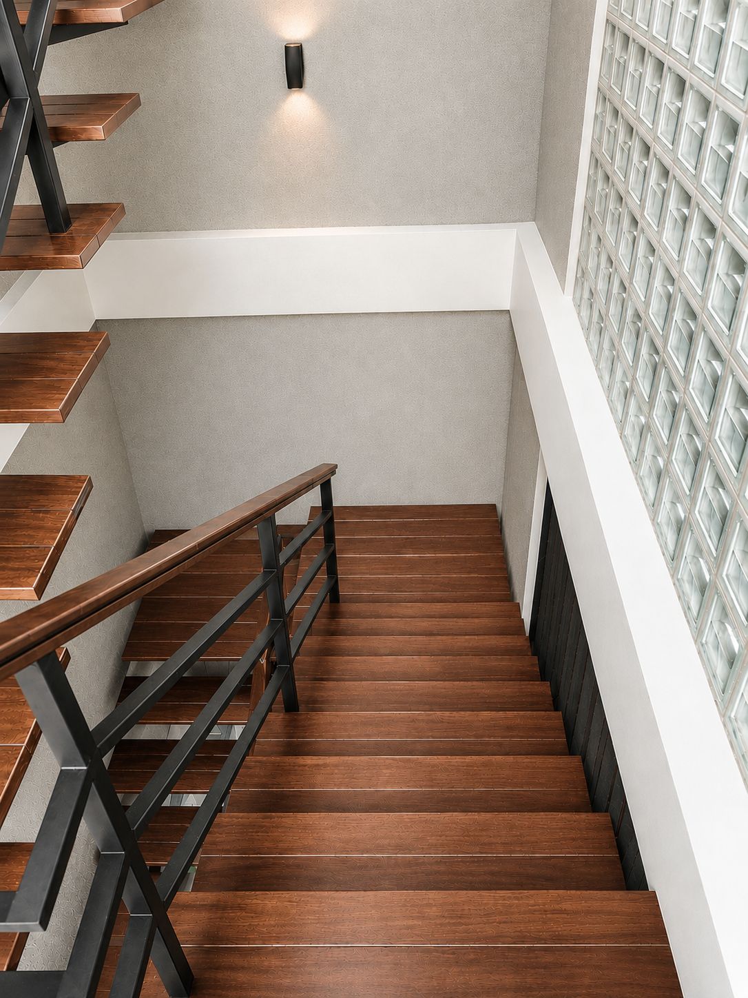 A staircase with wooden steps and metal railings, leading to a landing with a textured wall and a light fixture.