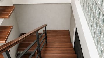 A staircase with wooden steps and metal railings, leading to a landing with a textured wall and a light fixture.