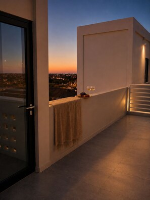 Un balcón con vista a un atardecer, una toalla y dos copas de vino.