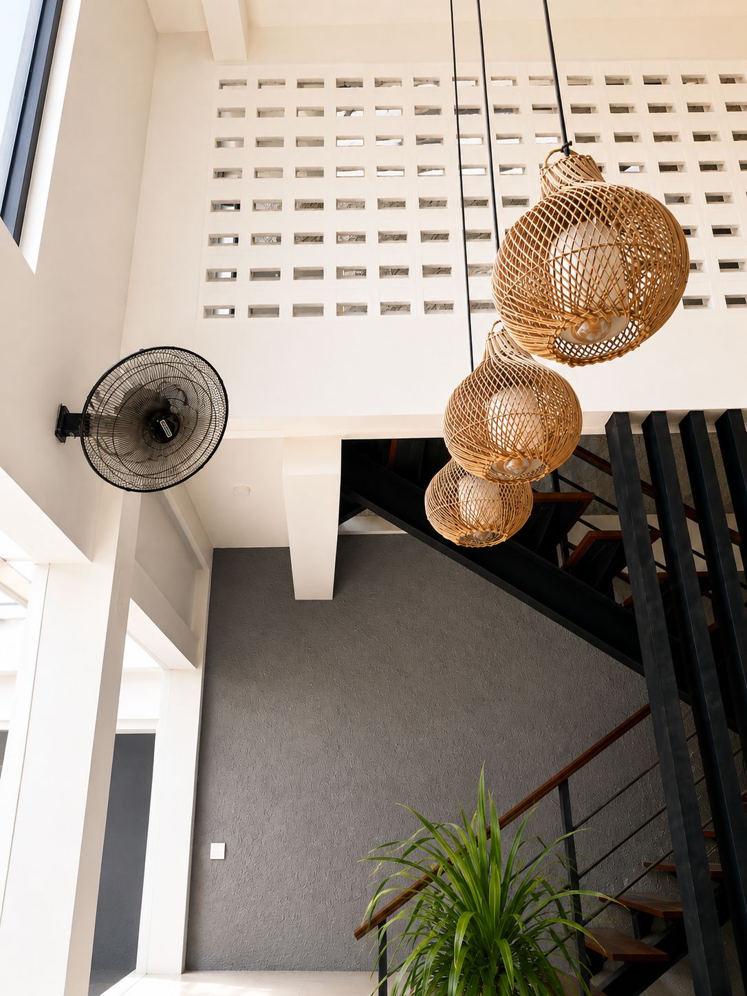 A modern interior with a staircase, a wall-mounted fan, and a hanging light fixture.