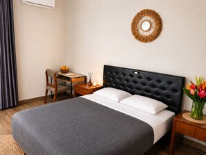 Habitación de hotel con cama, escritorio, silla, mesita de noche, aire acondicionado de pared y un adorno en la pared.