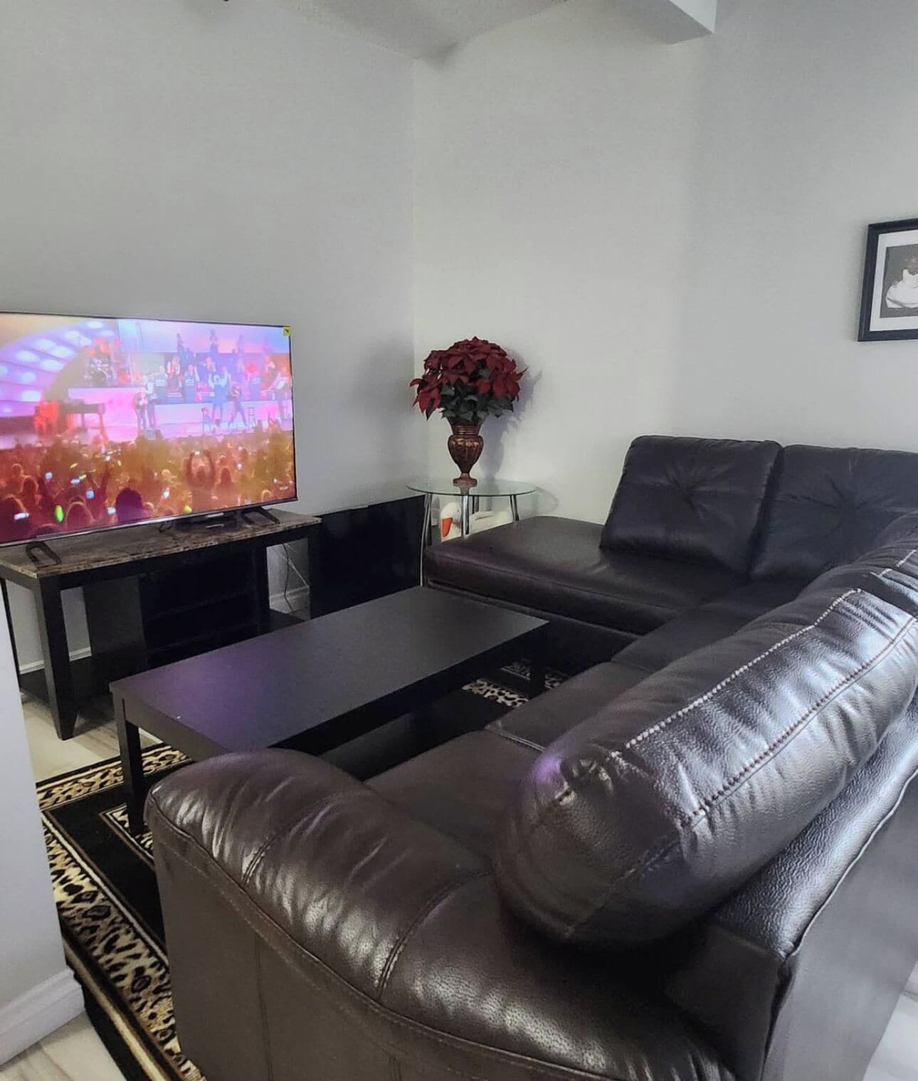 A living room with a leather sofa, a glass coffee table, and a television displaying a concert.
