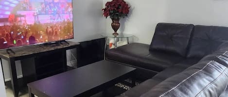 Un salon avec un canapé en cuir, une table basse en verre et un téléviseur diffusant un concert.