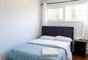 A neatly made bed with a patterned bedspread and pillows, a dark headboard, and a small bedside table with a lamp. - Room in Edmonton (Edmonton)
