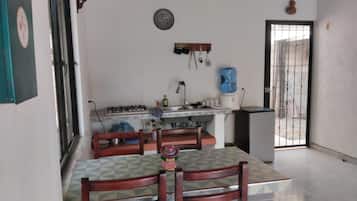 A kitchen with a gas stove, sink, and a water dispenser. There is a dining table with chairs and a decorative plate on the wall.