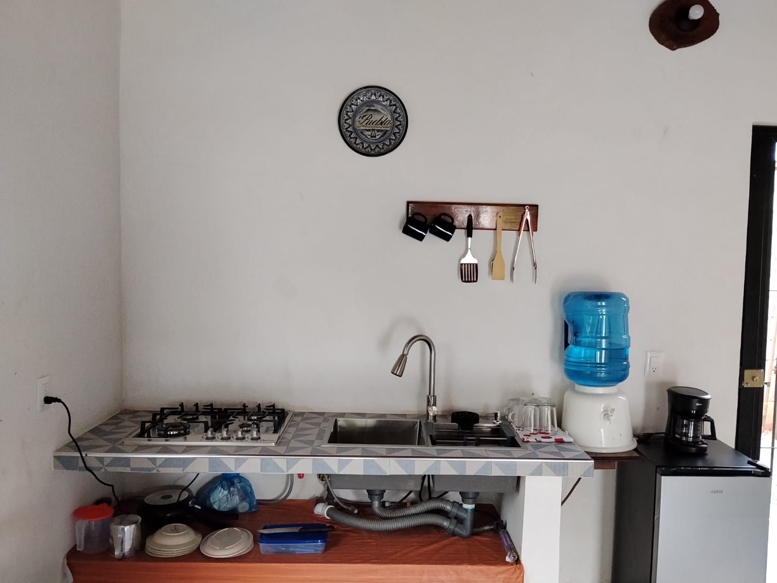 Une cuisine compacte équipée d’une cuisinière à gaz, d’un évier et d’un distributeur d’eau.