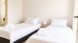 Hotellihuone, jossa on kaksi erillistä sänkyä, molemmissa valkoiset lakanat ja tyynyt, yöpöytä lampulla sekä ikkuna, josta on näkymä.
