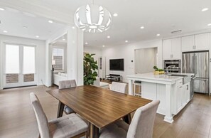 Una cocina moderna con armarios blancos, un refrigerador de acero inoxidable y una mesa de comedor de madera con sillas.