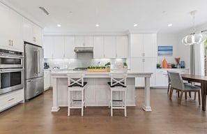 A modern kitchen with white cabinetry, stainless steel appliances, and a central island with two bar stools. - Irvine Orchard Hills 4B3B Great Home (Irvine)