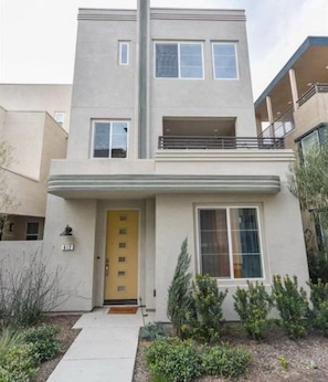 A two-story residential building with a flat roof, a balcony on the second floor, and a yellow front door. - Great Park Irvine 3B3.5B Family Home (Irvine)