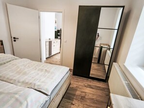 Ett sovrum med en säng, en garderob, en spegel och utsikt över ett kök och ett badrum.