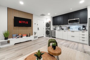 Un saló modern amb un televisor de pantalla plana, un panell de paret de fusta, un moble de televisió blanc i una taula de centre rodona de fusta amb una planta.