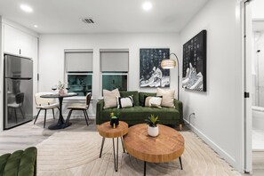 Una sala de estar moderna con un sofá verde, dos mesas redondas de madera y un ventanal grande.