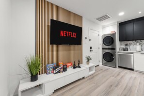 A modern kitchen with a built-in washer and dryer, a large flat-screen TV mounted on a wooden panel, and a white console table with decorative items. - 2-bedroom Duo apartment in marvelous Dallas with AC and fitness room (Dallas)