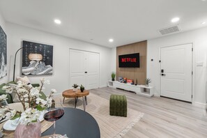 A modern living room with a flat-screen TV, a dining area with a table and chairs, and a cozy seating area with a green ottoman. - 2-bedroom Duo apartment in marvelous Dallas with AC and fitness room (Dallas)