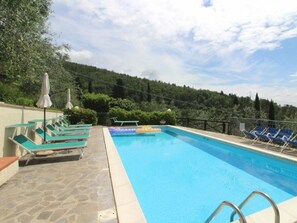 A swimming pool with lounge chairs and umbrellas, surrounded by trees and a stone deck. - Villa Agriturismo Arcobaleno (Loro Ciuffenna)