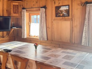 L’intérieur d’un chalet en bois, avec un téléviseur, une fenêtre avec des rideaux, un tableau accroché au mur et une table avec un set de table.
