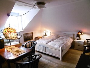 A bedroom with a bed, bedside tables, a lamp, a chair, a table, and a decorative lamp on a stand. - Holiday Apartment With 1 Bedroom (Lindau)