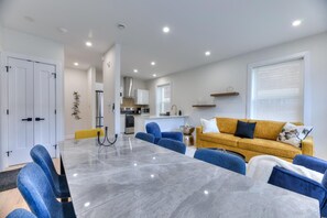 A modern living room with a marble table, blue chairs, a yellow sofa, and a kitchen in the background. - Westmount Gem 3BR • A/C • Wi-Fi • Laundry Inside • Near Metro & Parks (Westmount)