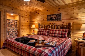 A cozy wooden room with a bed, a nightstand, a lamp, and a wall with a bear picture. - Sleeps 8, Private Mini Golf, Hot Tub, Arcade, Log Cabin, 9 Mi to Dollywood (Sevierville)