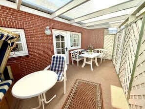 A covered patio with a brick wall, a white door, and a seating area with a table and chairs. - North Sea Room 03 (Nieblum)