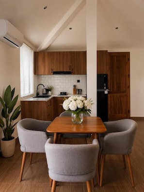Une cuisine moderne avec des meubles en bois, un réfrigérateur noir et un coin repas comprenant une table et deux chaises.