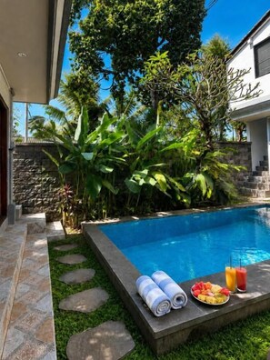 A swimming pool with a stone border, surrounded by lush greenery and a stone wall. - 1 Bedroom Norke Villa Gianyar (Gianyar)