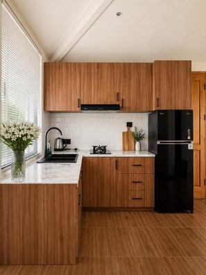 A kitchen with wooden cabinets, a black refrigerator, and a white countertop. - 1 Bedroom Norke Villa Gianyar (Gianyar)