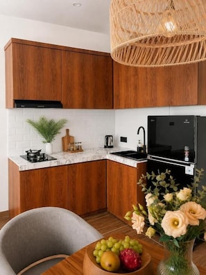 Une cuisine moderne avec des meubles en bois, un plan de travail en marbre, un réfrigérateur noir et un coin repas comprenant une table et des chaises.