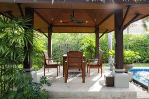 Un área de estar al aire libre techada con mobiliario de madera y una piscina.