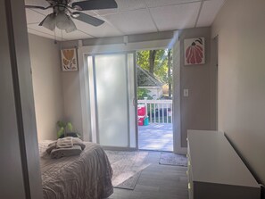 A bedroom with a bed, a ceiling fan, a sliding glass door leading to a deck, and a small plant. - Charming 4-bedroom duplex (Manchester)