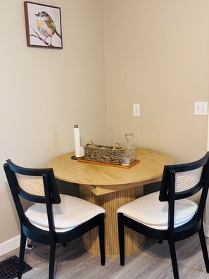 A round wooden table with two black chairs, a wicker basket, a glass jar, and a framed picture of a bird on the wall. - Charming 4-bedroom duplex (Manchester)