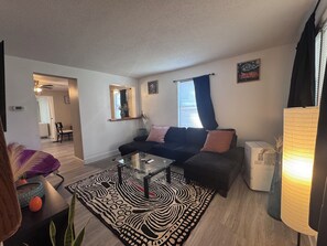 A living room with a black sofa, a glass coffee table, a patterned rug, a small plant, and a lamp. - Charming 4-bedroom duplex (Manchester)