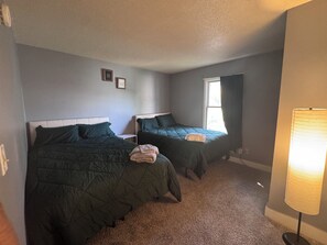 A bedroom with two beds, a bedside table, a lamp, and a window. - Charming 4-bedroom duplex (Manchester)